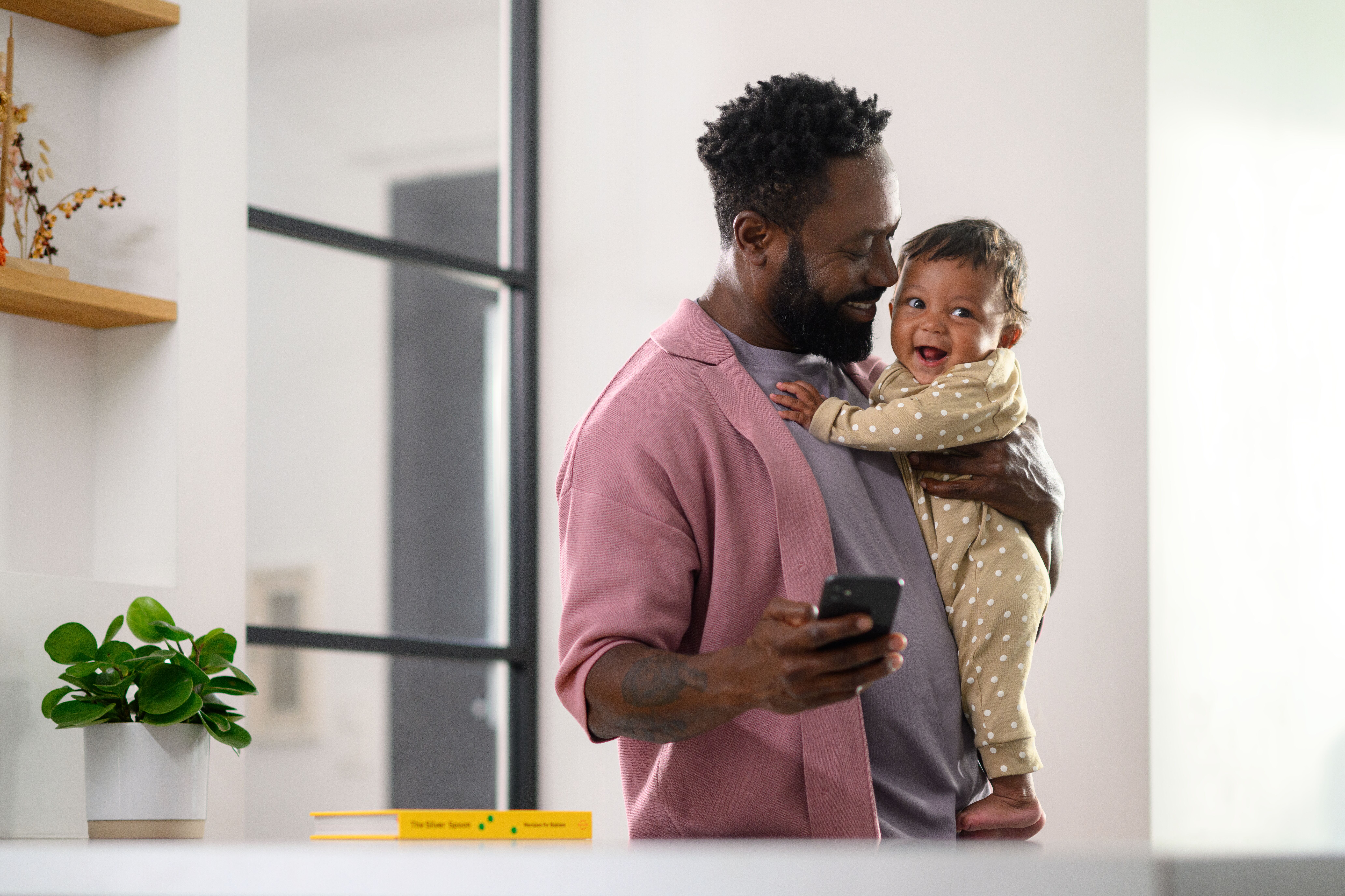 JPG RGB 300 DPI-MC_2023_maxicosi_ConnectedHome_General_Lifestyle_Kitchen_Dadholdingbabyandcheckinghisphotne_Landscape.jpg